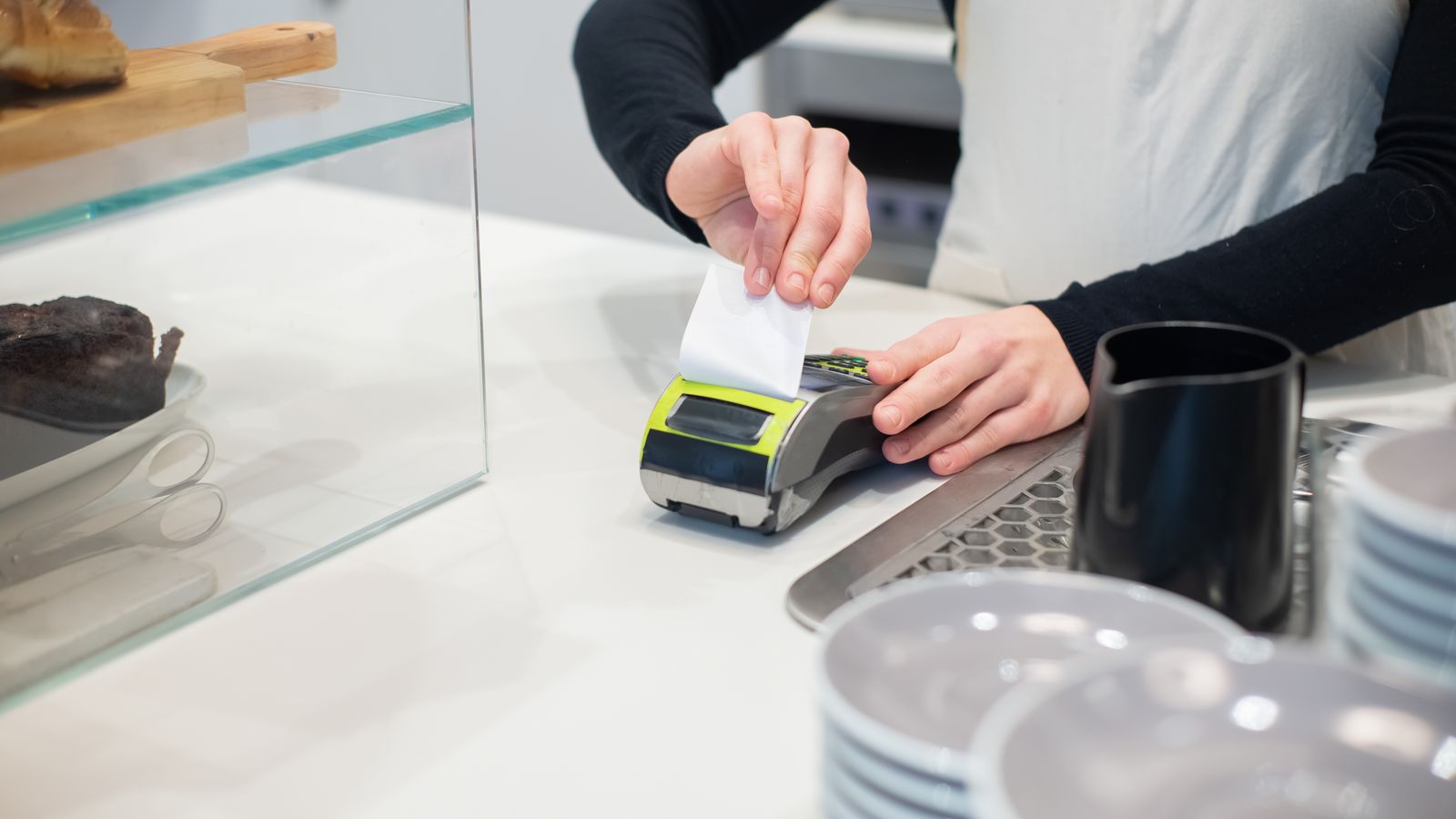 Shopkeeper handing a receipt to a customer at the counter, illustrating the simplified invoice for small amounts in Belgium