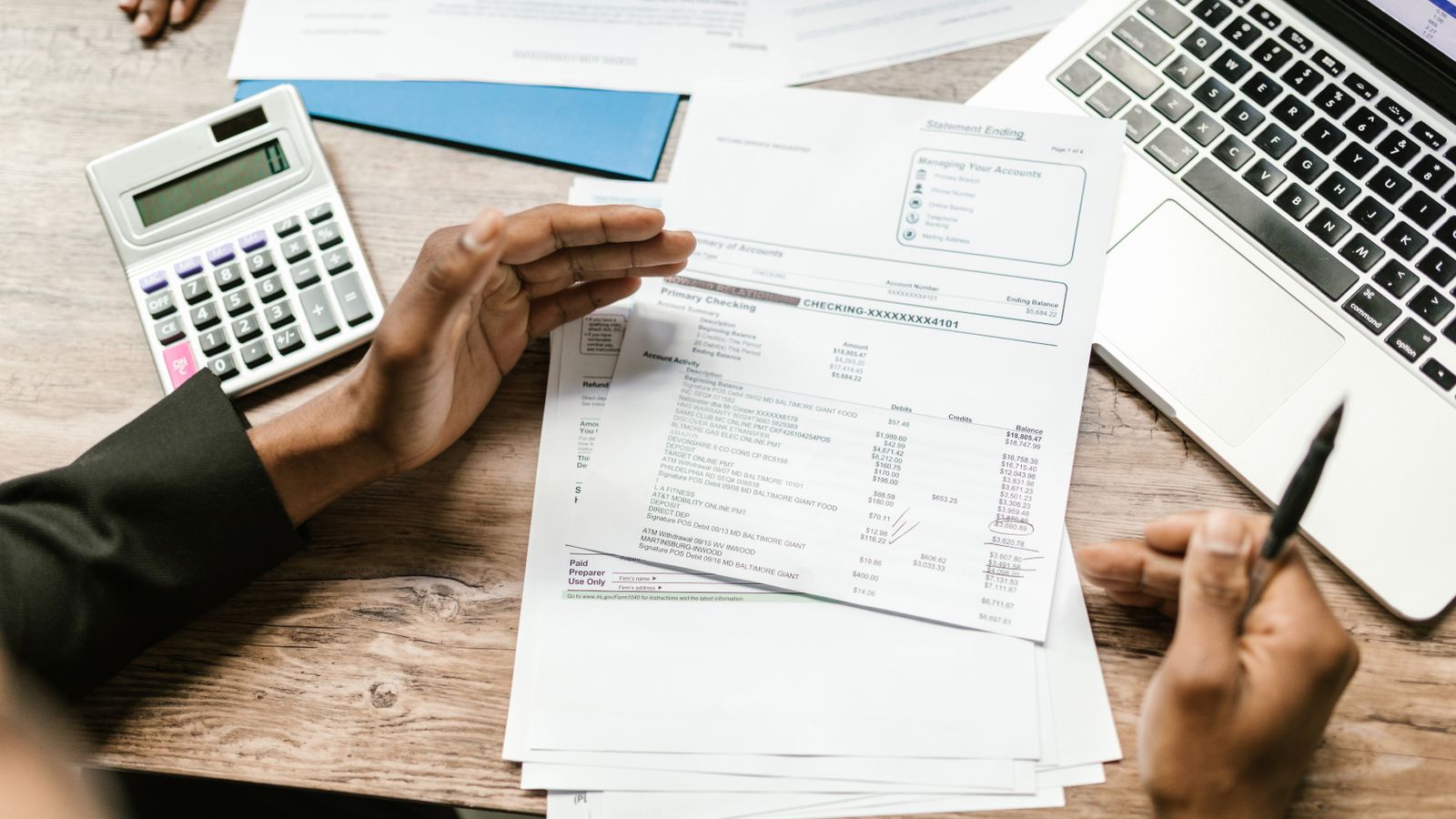 Hands holding financial documents next to a calculator and laptop, illustrating the preparation of the annual VAT client listing